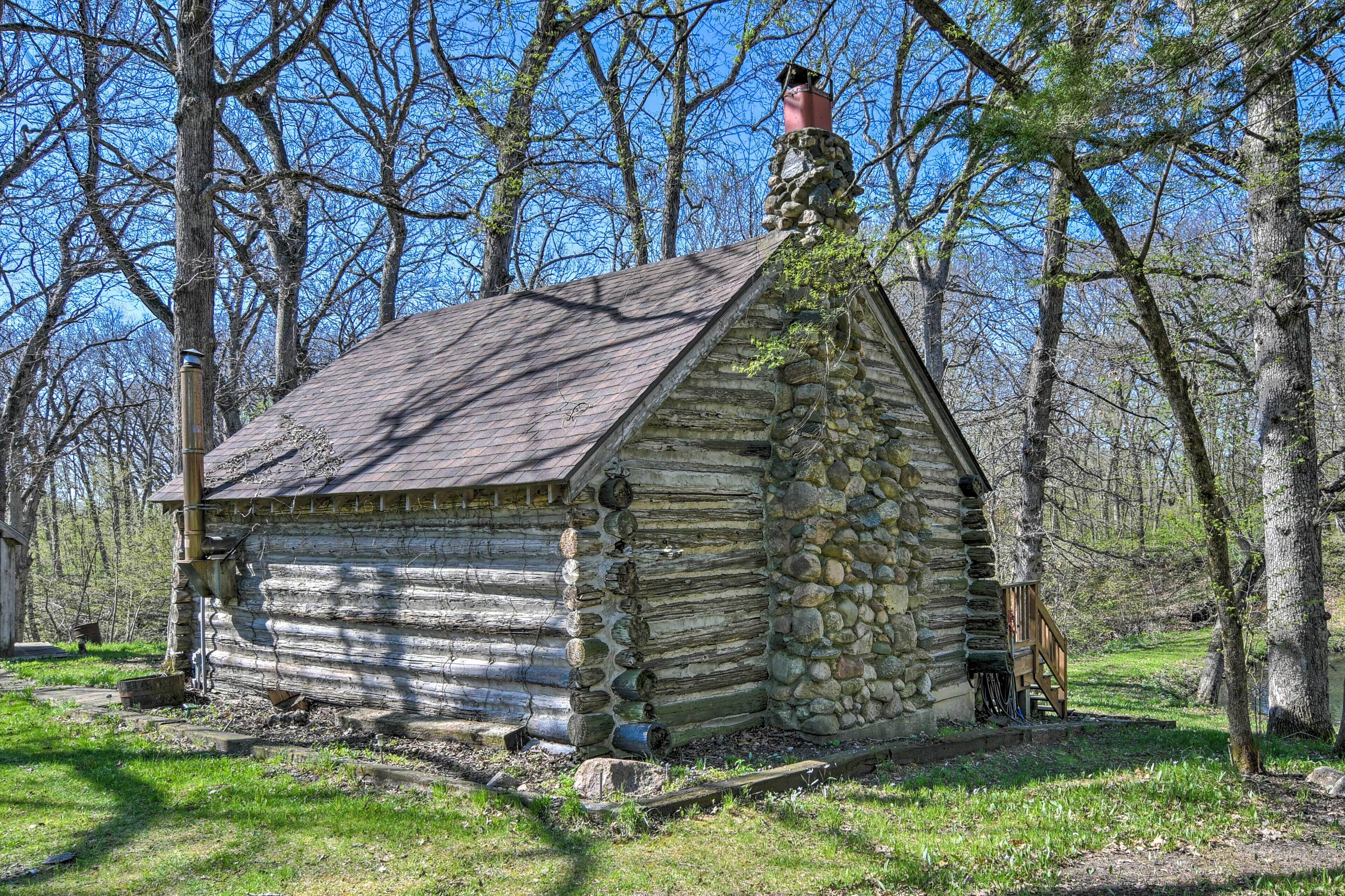 A rustic log cabin with a stone chimney, surrounded by trees.