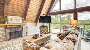 A spacious living room with a fireplace, a large sofa, and a television. - Flagstaff A-frame Cabin w/ Deck & Lovely Views! (Flagstaff)