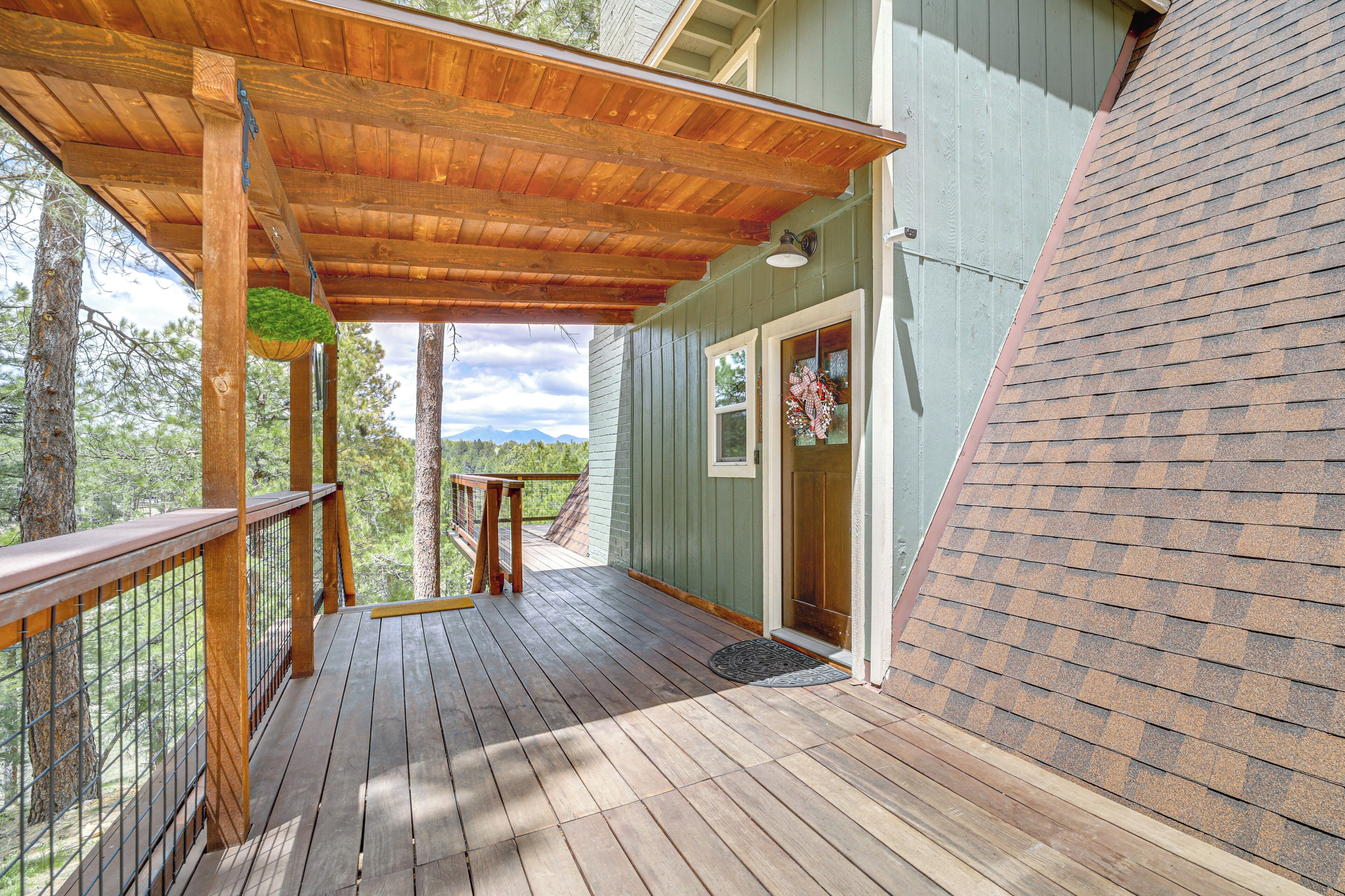 A wooden deck with a pergola, a door with a wreath, and a view of trees and mountains.