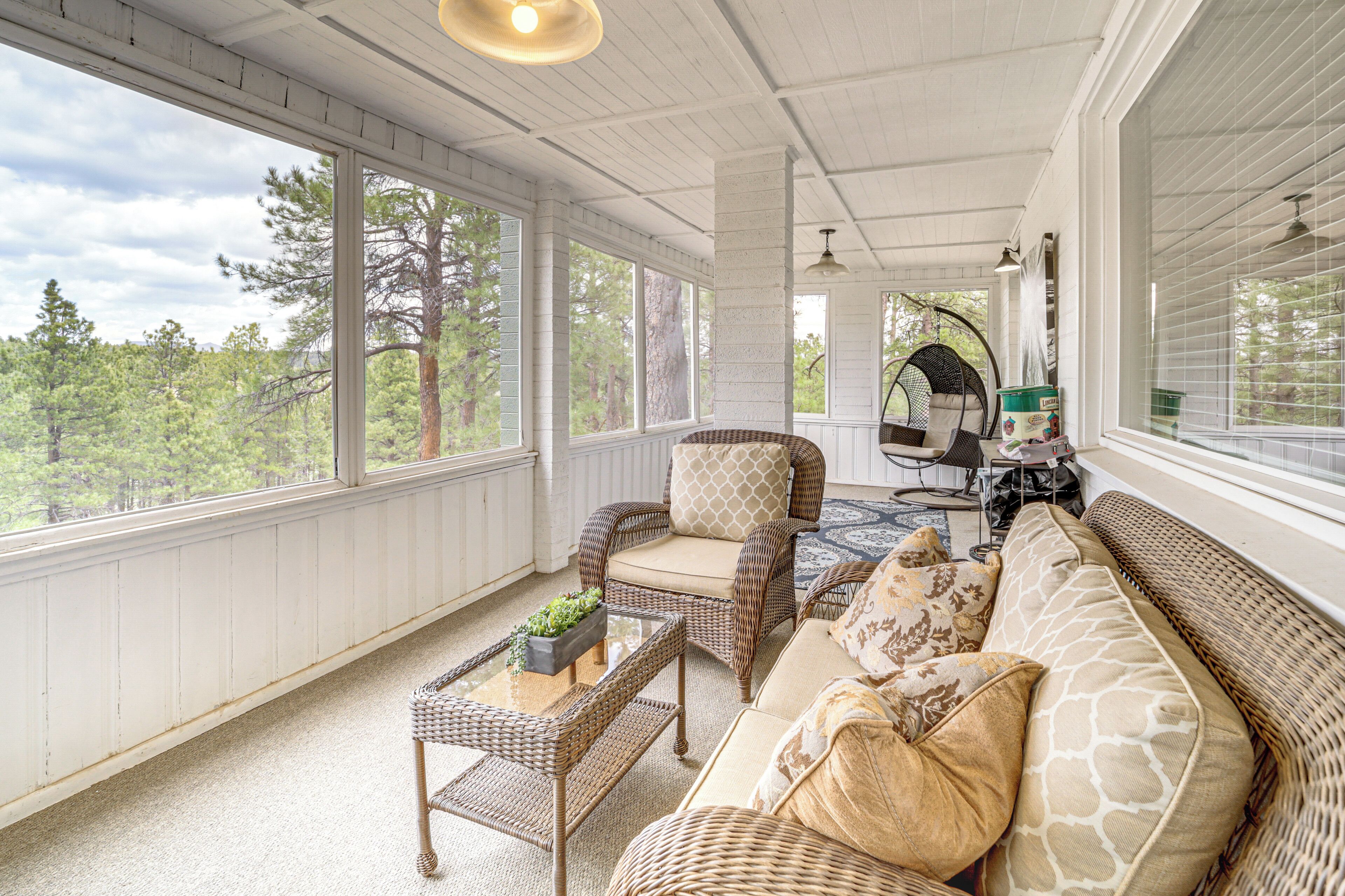 Ein überdachter Balkon mit Korbmöbeln, großen Fenstern und Blick auf Bäume.