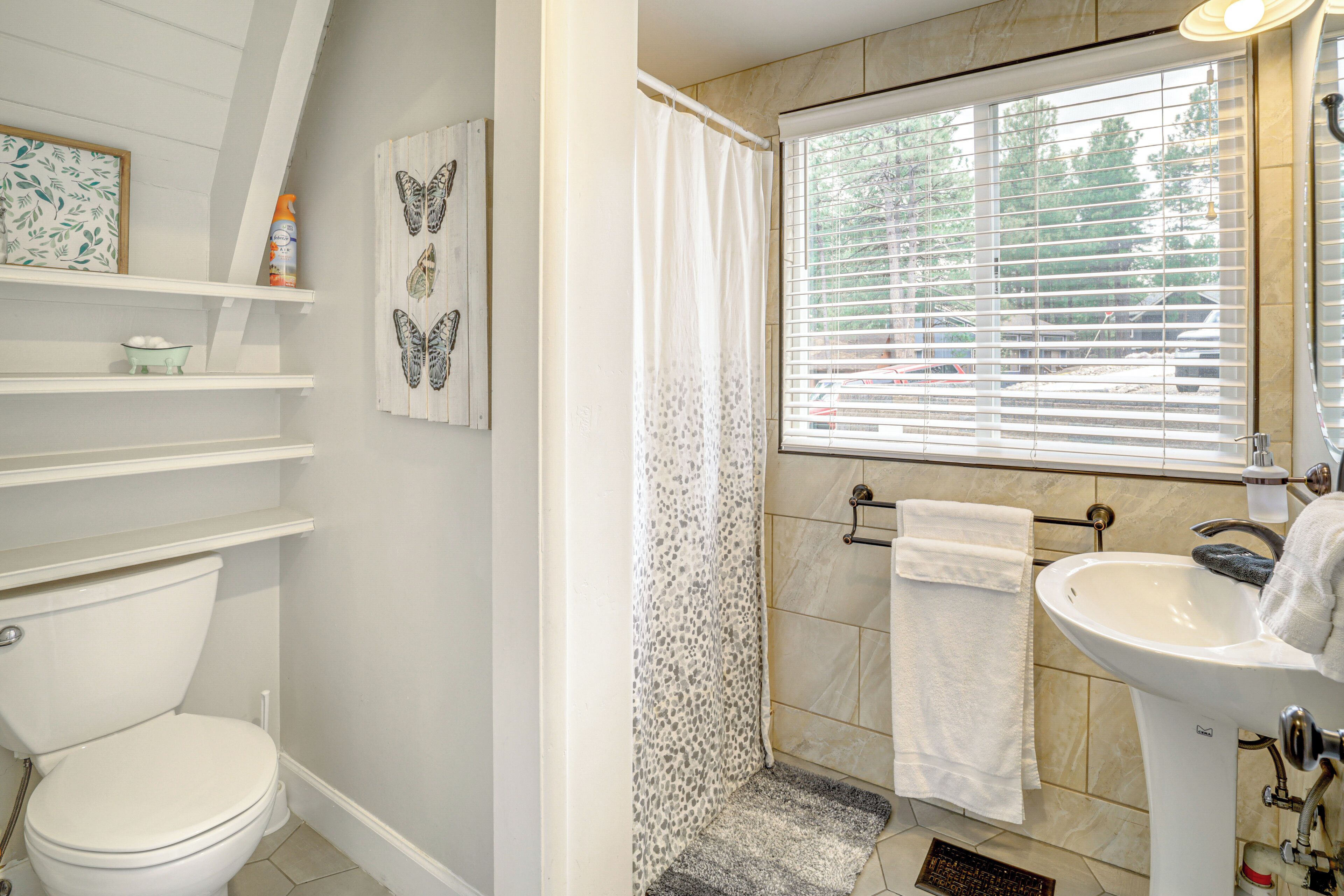 A bathroom with a toilet, shower, sink, and a window with blinds.