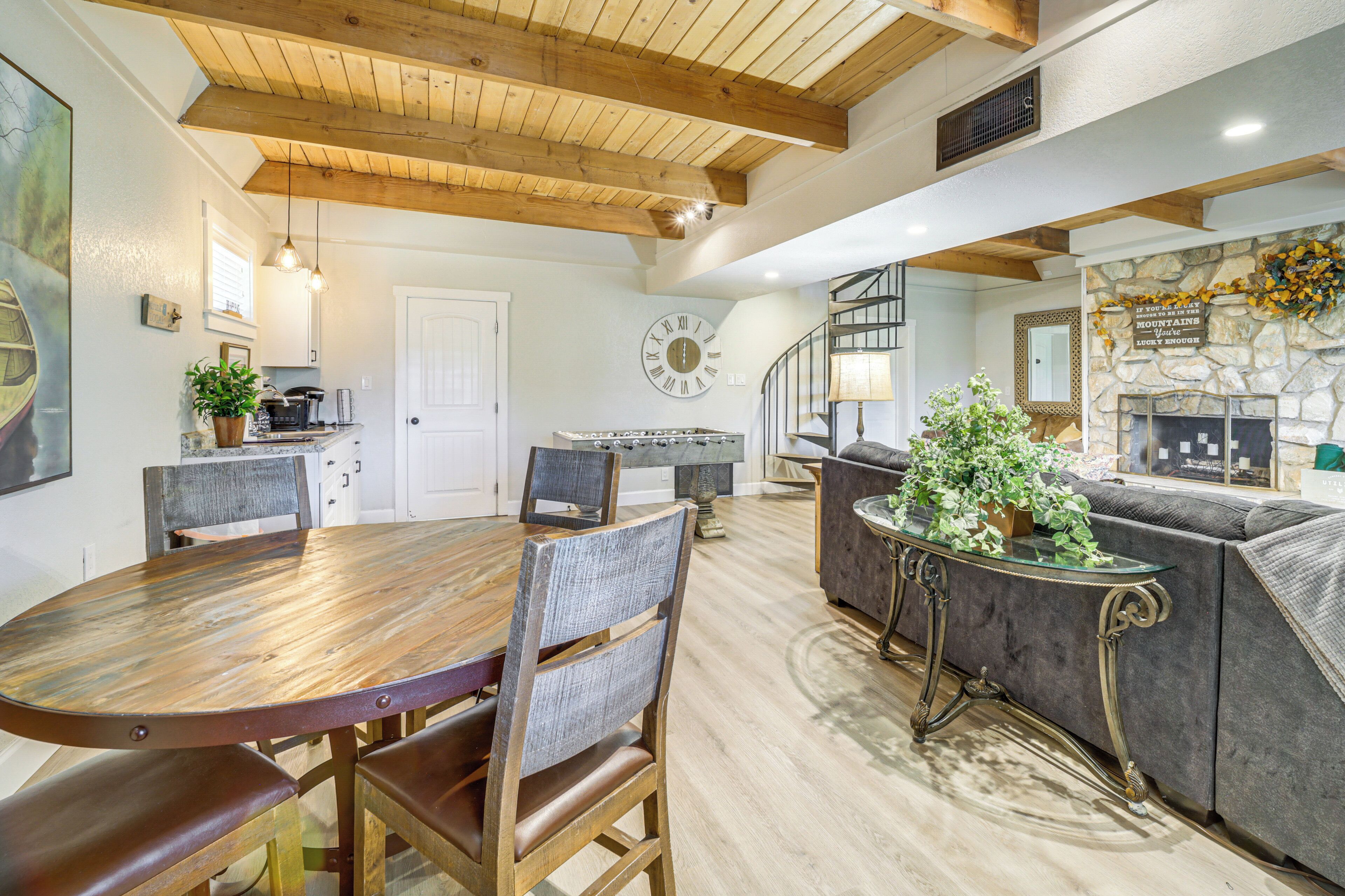 A spacious living area with a wooden dining table, comfortable seating, a stone fireplace, and a modern kitchen in the background.