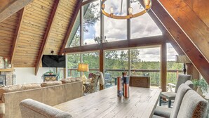 A spacious dining area with a wooden table and multiple chairs, large windows offering a view of the outdoors, and a high ceiling with exposed beams. - Flagstaff A-frame Cabin w/ Deck & Lovely Views! (Flagstaff)