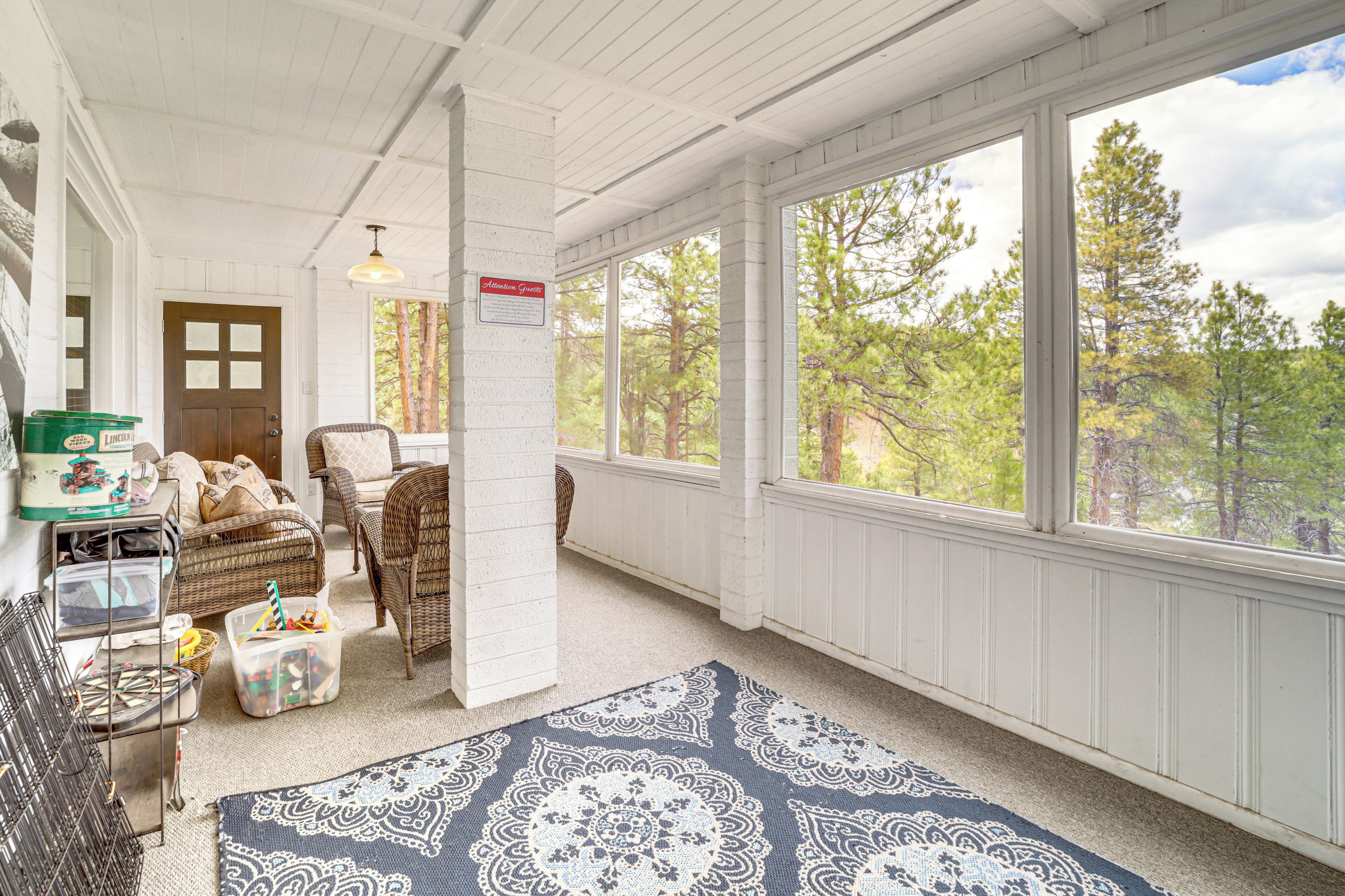 Une pièce chaleureuse avec une grande fenêtre, des meubles en osier et un tapis bleu à motifs.