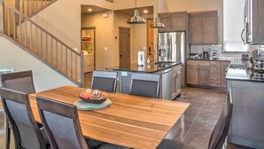 A modern kitchen with a central island, stainless steel appliances, and a dining area with a wooden table and chairs. - Upscale Moab Home w/ Red Rock Views & Hot Tub (Moab)