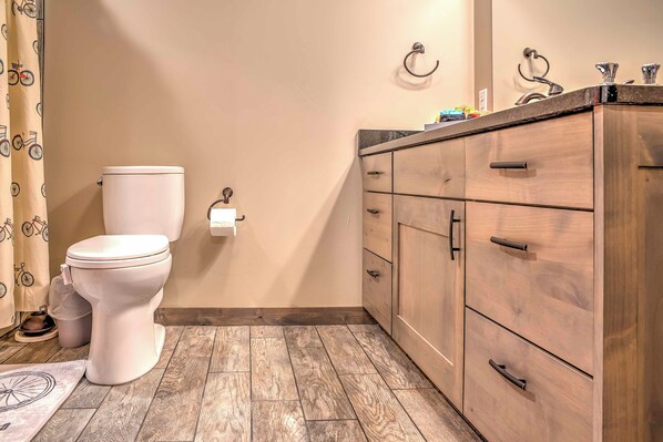 A bathroom with a toilet, wooden cabinets, and a patterned shower curtain. - Upscale Moab Home w/ Red Rock Views & Hot Tub (Moab)