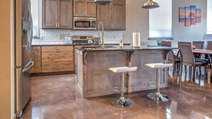 A modern kitchen with wooden cabinets, stainless steel appliances, and a central island with bar stools. - Upscale Moab Home w/ Red Rock Views & Hot Tub (Moab)
