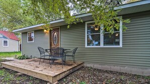 Une maison avec une terrasse en bois, une porte ornée d’un panneau décoratif et une fenêtre avec des stores.
