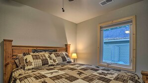 A bedroom with a large bed, a window with blinds, and a wooden headboard. - Pet-friendly Petoskey Area Cabin, Walk to River! (Alanson)