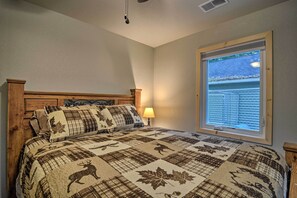 A bedroom with a large bed, a window with blinds, and a wooden headboard. - Pet-friendly Petoskey Area Cabin, Walk to River! (Alanson)