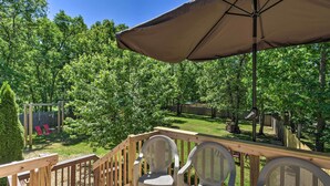 A wooden deck with chairs and an umbrella, overlooking a backyard with a swing set and trees.