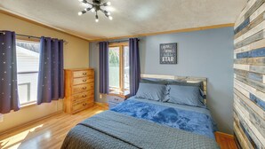 A bedroom with a wooden headboard, a bed with a blue and white patterned bedspread, a wooden dresser, and a ceiling light fixture.