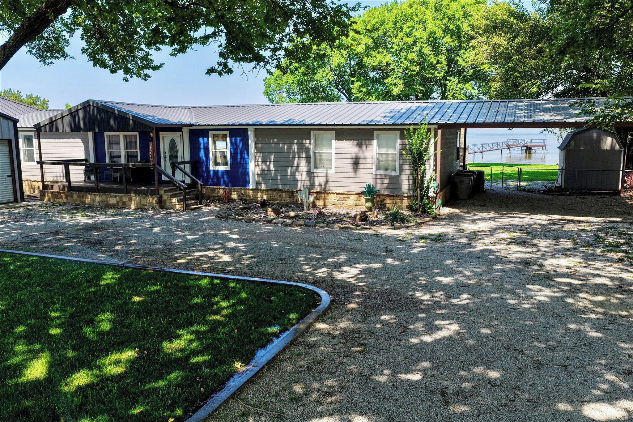 A building with a covered porch, a gravel driveway, and a fenced area with a dock.