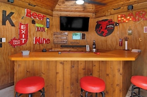 A bar area with a wooden interior, a television mounted on the wall, and three red bar stools.
