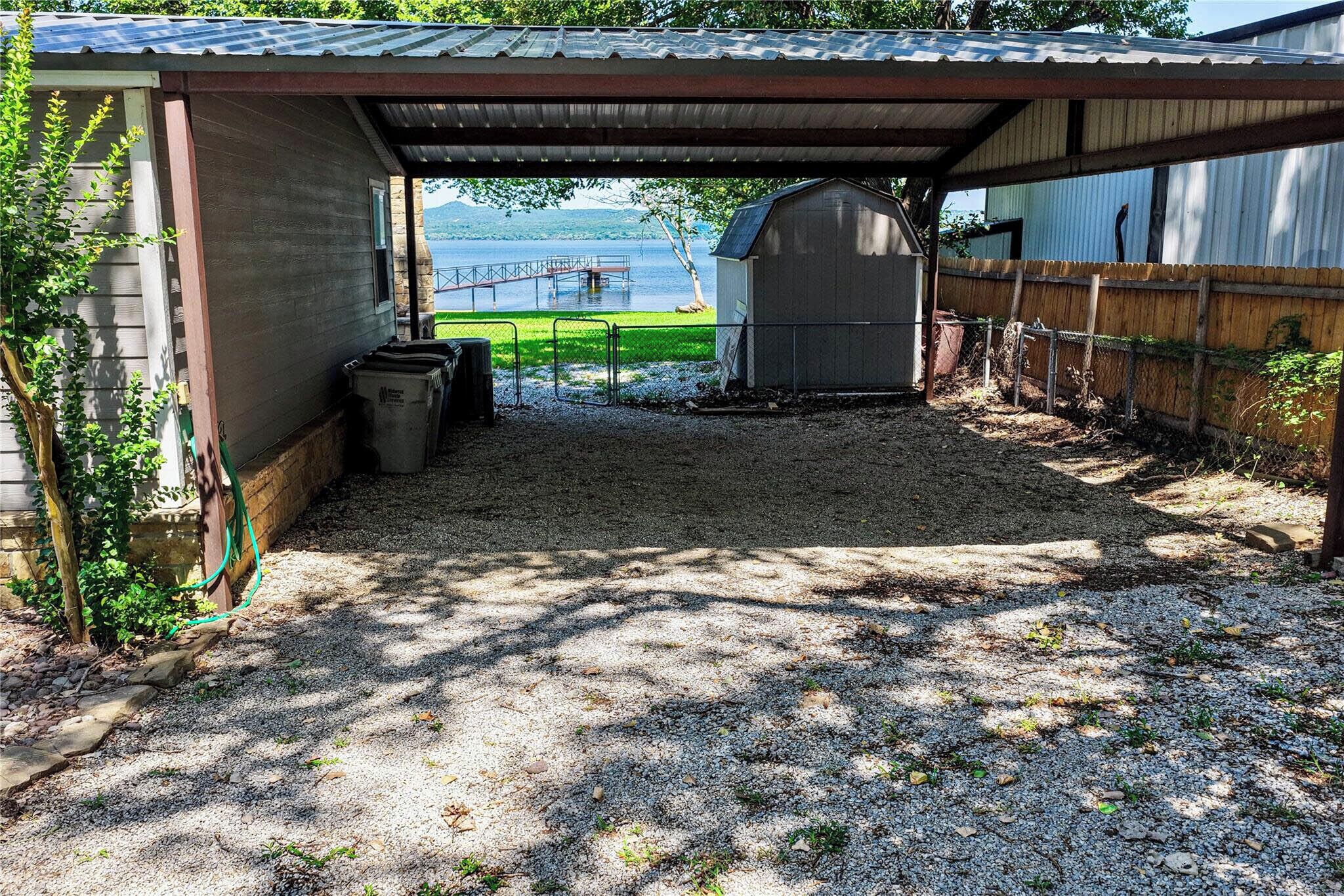 A covered outdoor area with a gravel floor, a metal fence, and a view of a body of water.