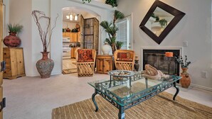 Un salon avec une table basse en verre, des chaises en bois, une cheminée et un miroir au mur.