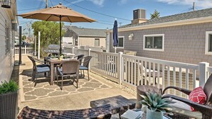 Eine Terrasse im Freien mit Tisch, Stühlen und einem großen Sonnenschirm, umgeben von einem weißen Zaun.