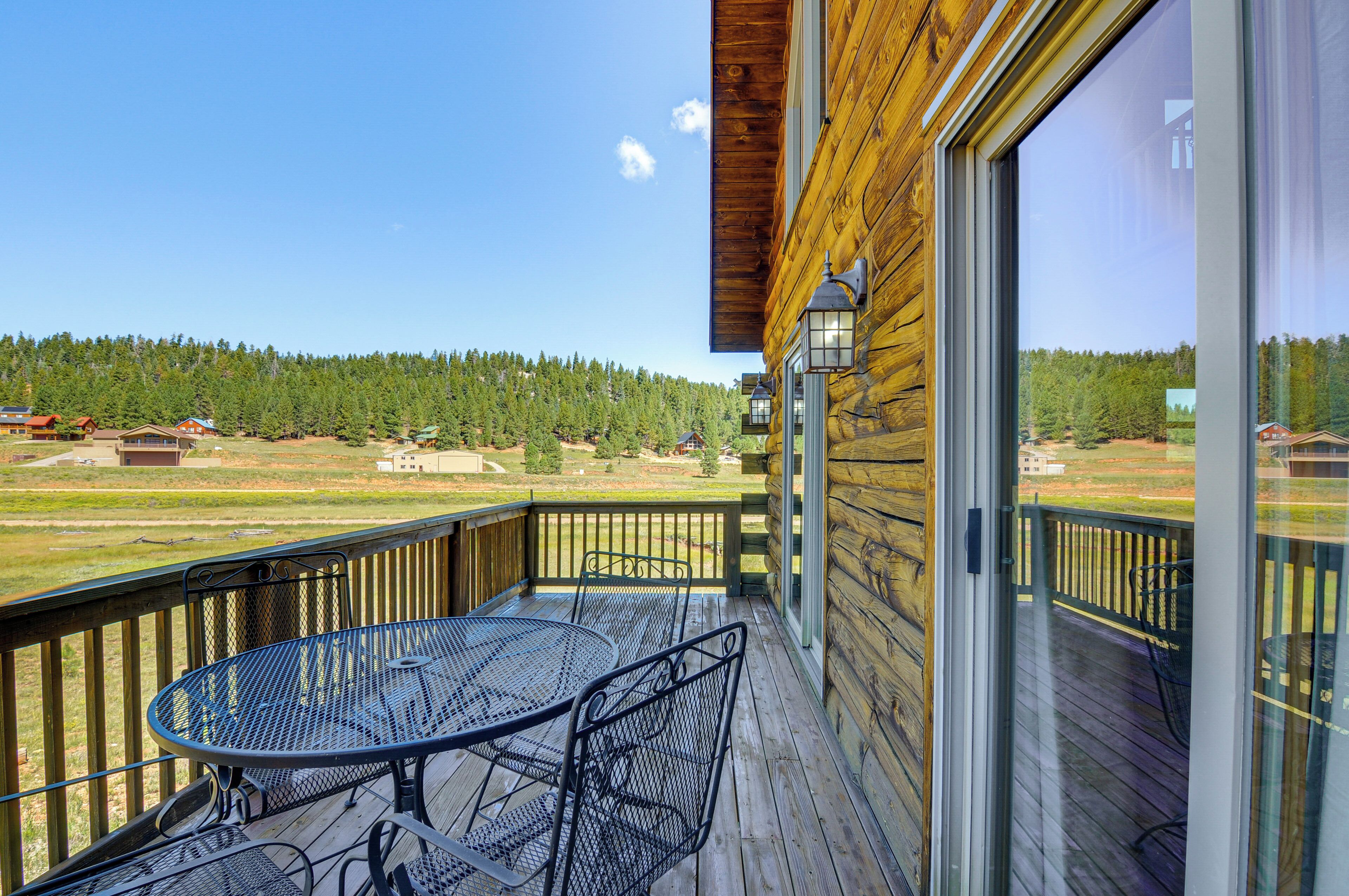 A wooden deck with a table and chairs, overlooking a forested area.