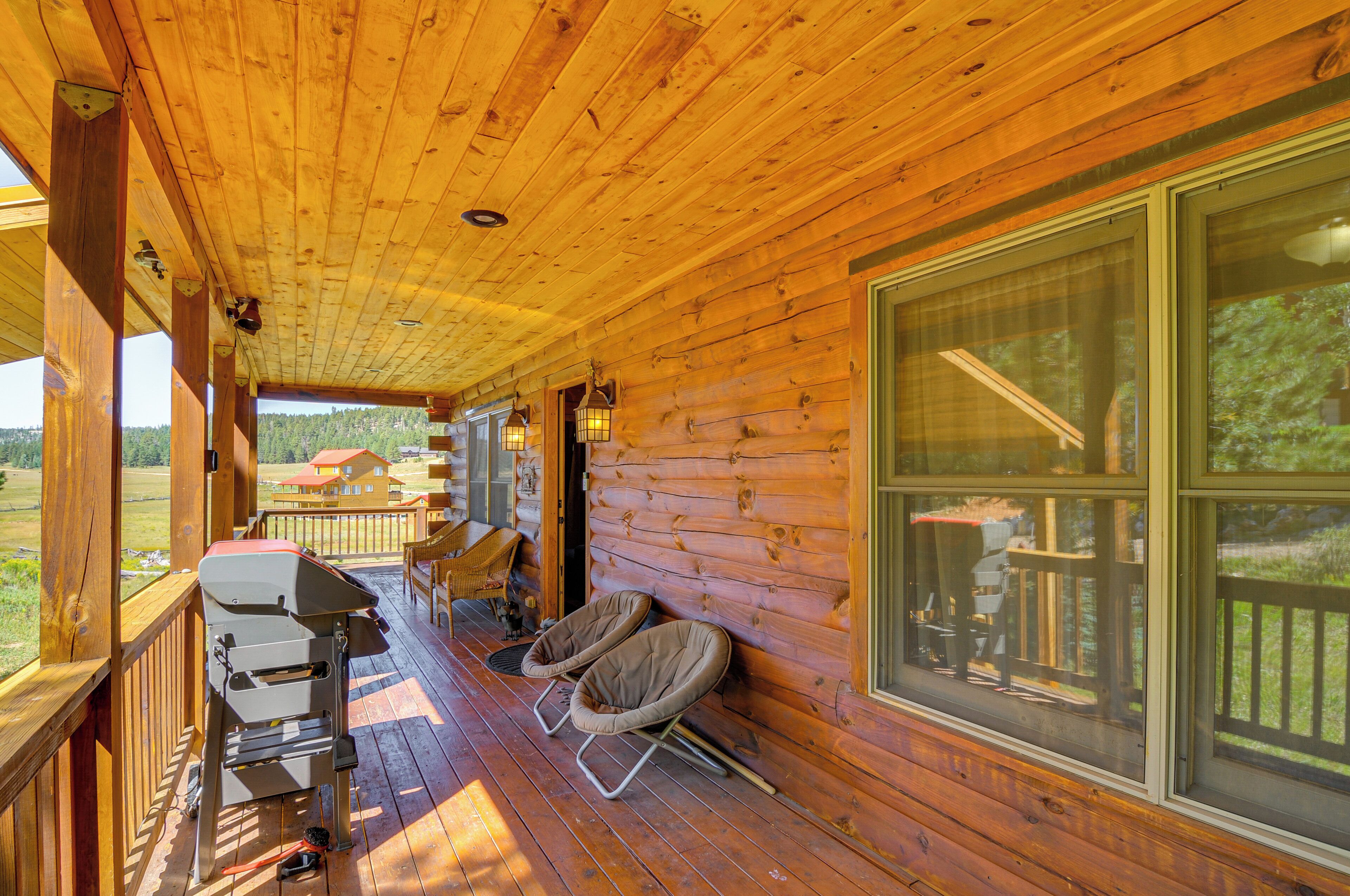 A wooden cabin with a porch, a grill, and two chairs.