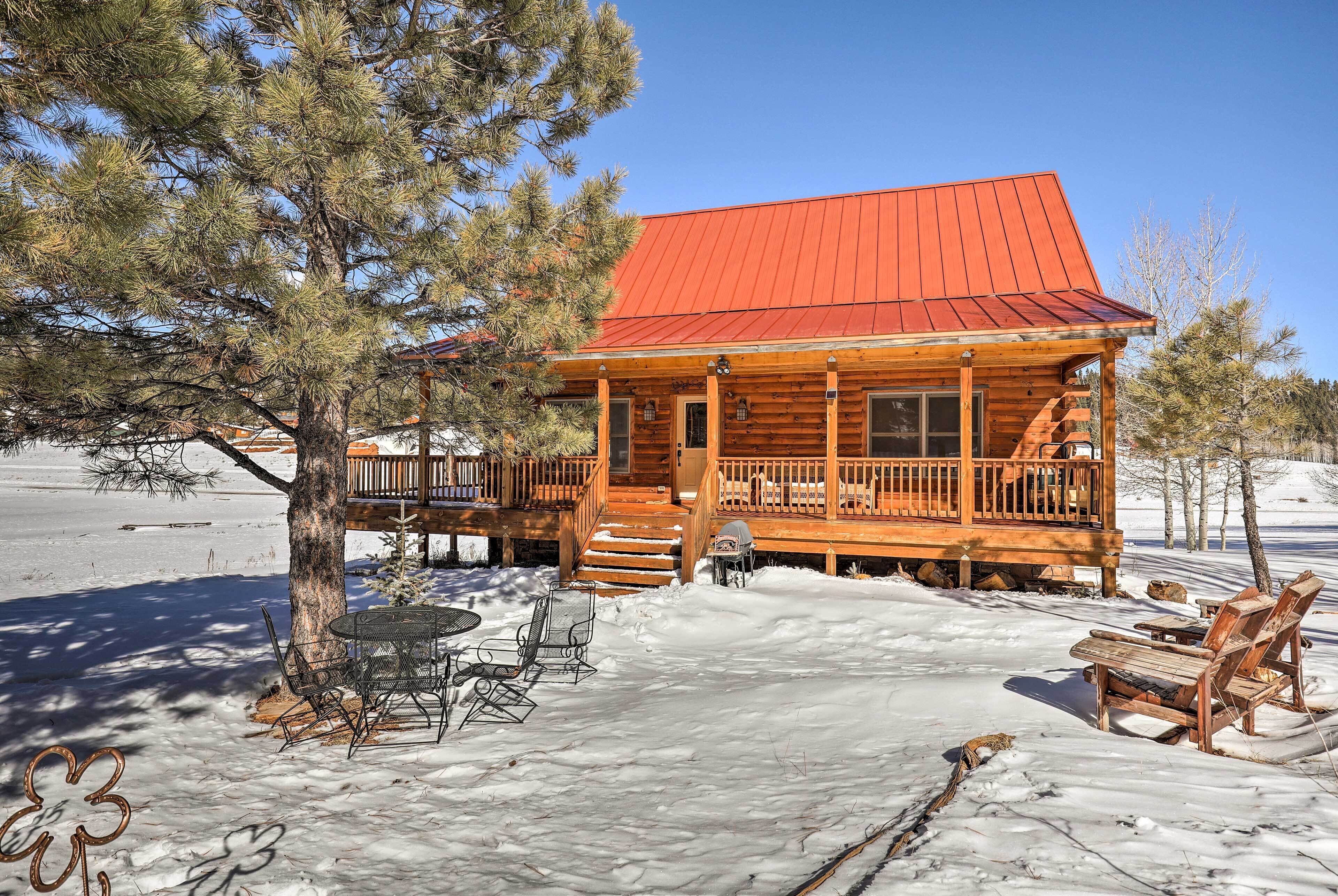 A log cabin with a red roof, wooden deck, and outdoor seating area.