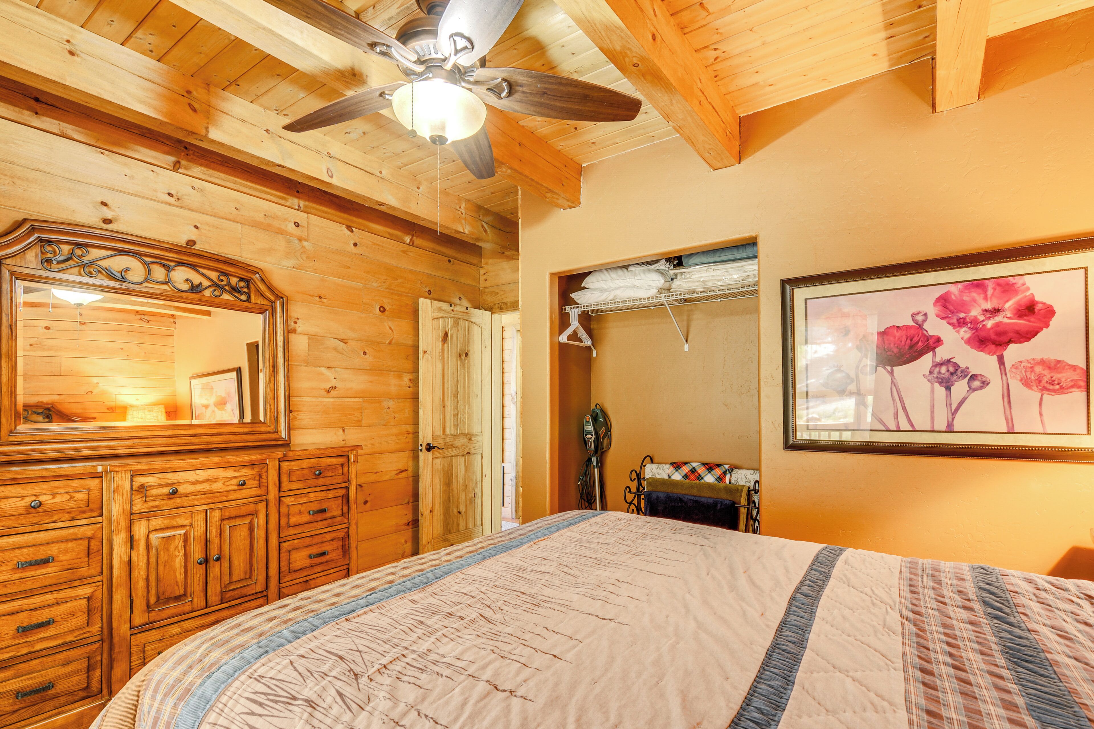 A wooden room with a bed, a dresser, a ceiling fan, and a framed picture on the wall.