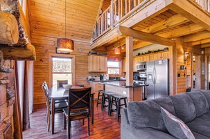 A log cabin interior with a dining area, kitchen, and a living room with a sofa.