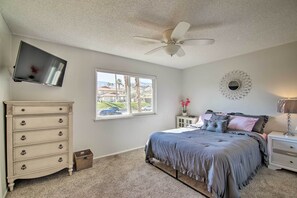 A bedroom with a bed, dresser, TV, window, and ceiling fan.