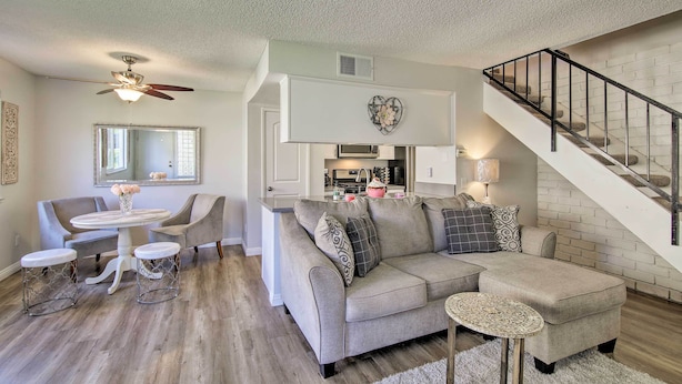 A spacious living room with a grey sofa, a dining table with chairs, a ceiling fan, and a staircase. - Palm Desert Resort-style Living: Dog Friendly (Palm Desert)