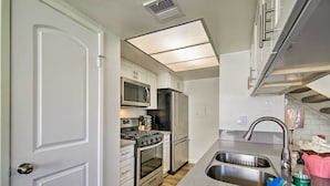 A compact kitchen with a stainless steel sink, a microwave, a stove, and a refrigerator. - Palm Desert Resort-style Living: Dog Friendly (Palm Desert)