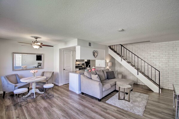 A modern living room with a sofa, coffee table, and a dining area with chairs. There is a staircase leading to an upper level.