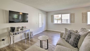 A modern living room with a flat-screen TV, a glass coffee table, and a grey sofa with patterned cushions. - Palm Desert Resort-style Living: Dog Friendly (Palm Desert)