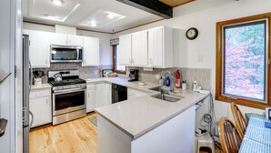 A modern kitchen with white cabinets, stainless steel appliances, and a large window with a view of trees. - Community Perks: Retreat w/ Thirteenth Lake Access (North River)