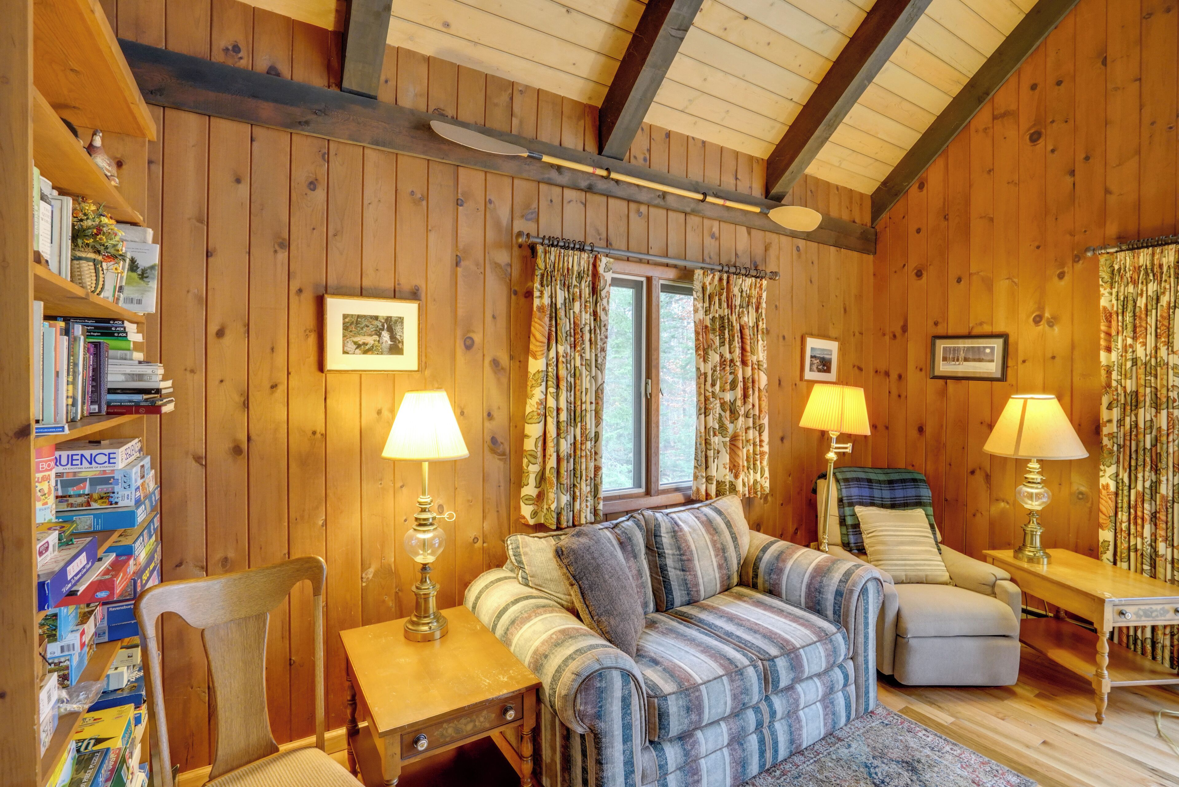 Una habitación acogedora de madera con un sofá a rayas, una silla, una mesita y una estantería llena de libros.