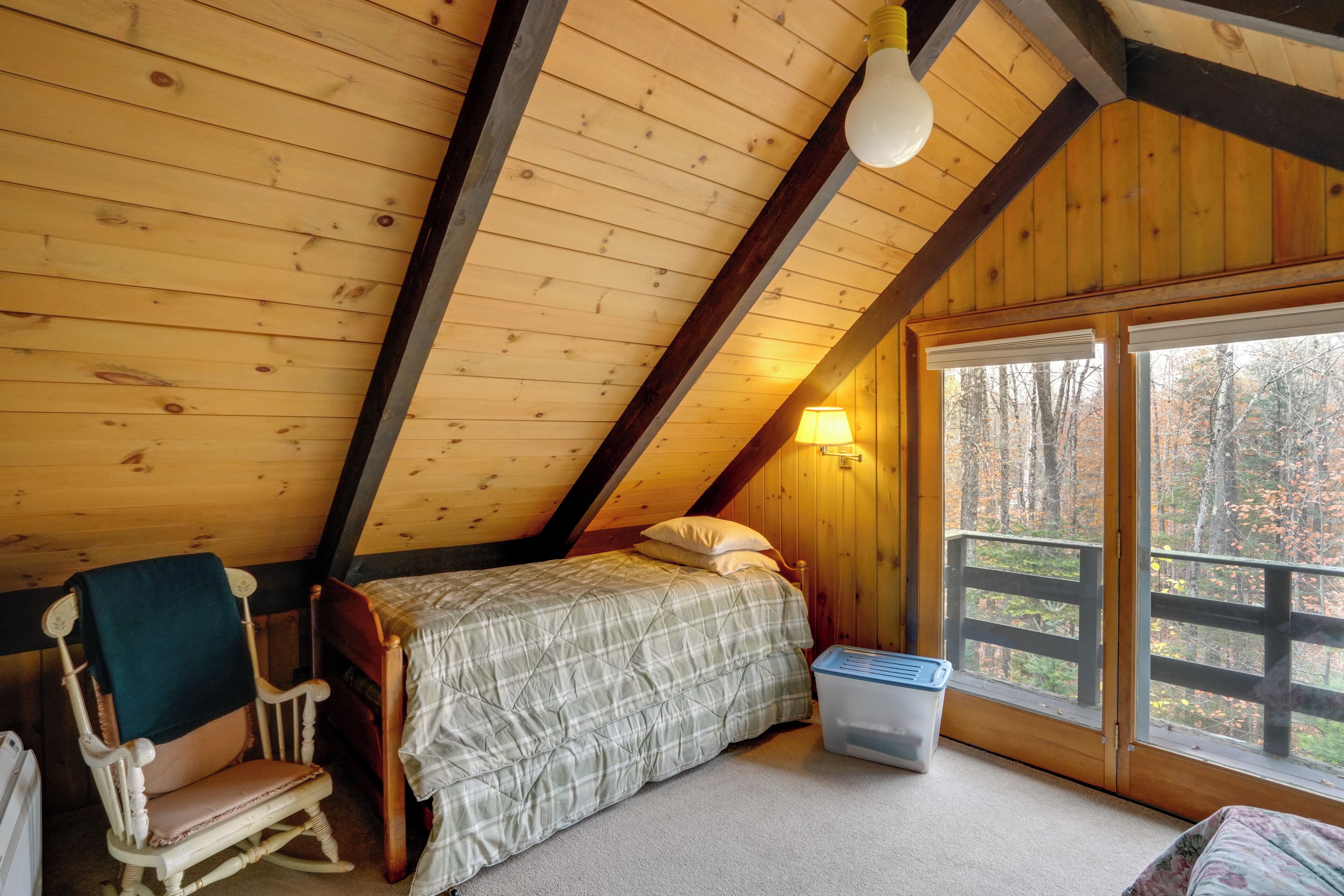 A cozy attic bedroom with a bed, rocking chair, and a window with a view of trees.