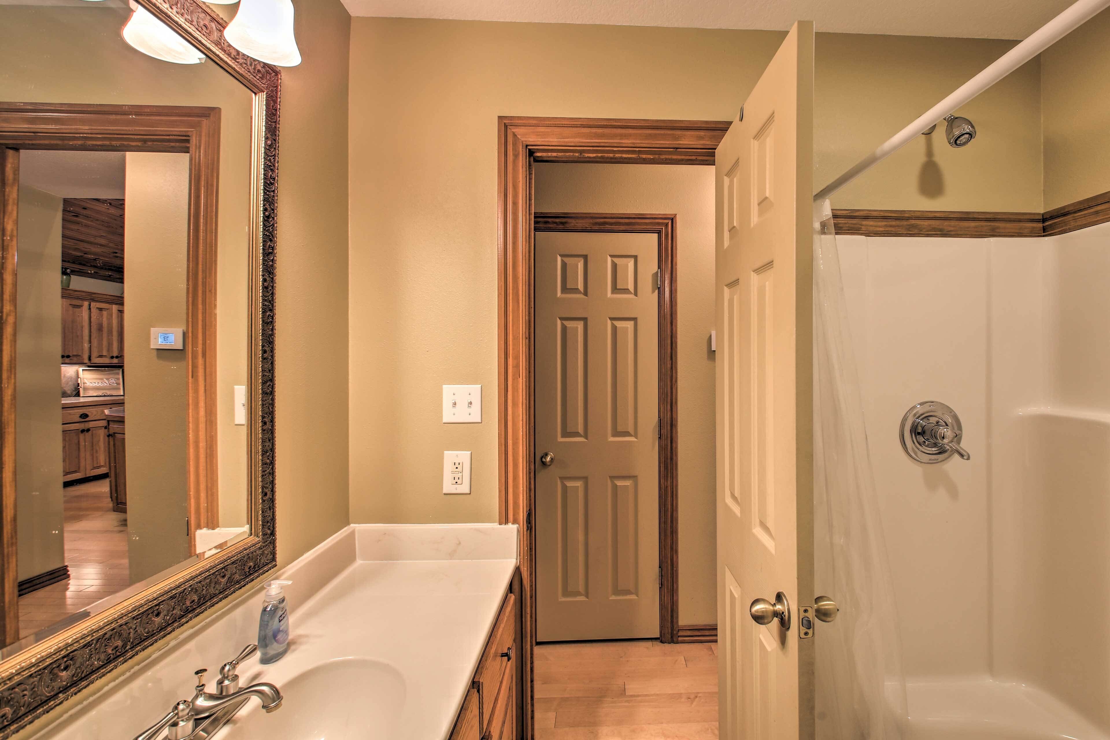 A bathroom with a bathtub, a sink with a mirror, and a door leading to another room.