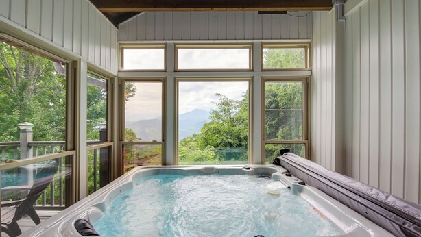 Ein Whirlpool mit Blick auf eine gebirgige Landschaft durch große Fenster.