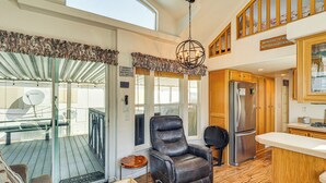 A spacious living area with a leather recliner, a kitchen with wooden cabinets, and a large window overlooking a deck. - Boat Launch + Mtn Views: Lake Havasu Cabin (Lake Havasu City)