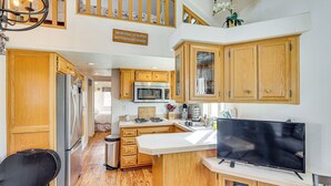 A kitchen with wooden cabinets, a stainless steel refrigerator, a microwave, and a large flat-screen TV. - Boat Launch + Mtn Views: Lake Havasu Cabin (Lake Havasu City)