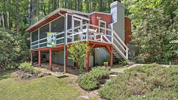 Eine Holzhütte mit Glasveranda, einer Holzterrasse und einer Treppe, die zu einer roter Tür führt.