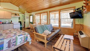 A cozy cabin interior with a wooden ceiling, a dining area with a table and chairs, a sofa with a quilt, and a kitchenette with a refrigerator and stove. - Secluded Nantahala 'gone Hunting' Cabin w/ Hot Tub (Bryson City)