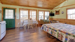A cozy cabin with a wooden ceiling, a green door, a dining table with chairs, a bed with a quilt, and a television on the wall. - Secluded Nantahala 'gone Hunting' Cabin w/ Hot Tub (Bryson City)