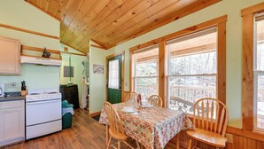 A cozy kitchen with wooden cabinets, a stove, and a dining area with a table set for two. - Secluded Nantahala 'gone Hunting' Cabin w/ Hot Tub (Bryson City)