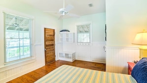A bedroom with a wooden floor, a striped rug, a ceiling fan, built-in shelving, and a window with blinds. - Waterfront Perdido Beach House w/ Canoes & Kayaks! (Elberta)