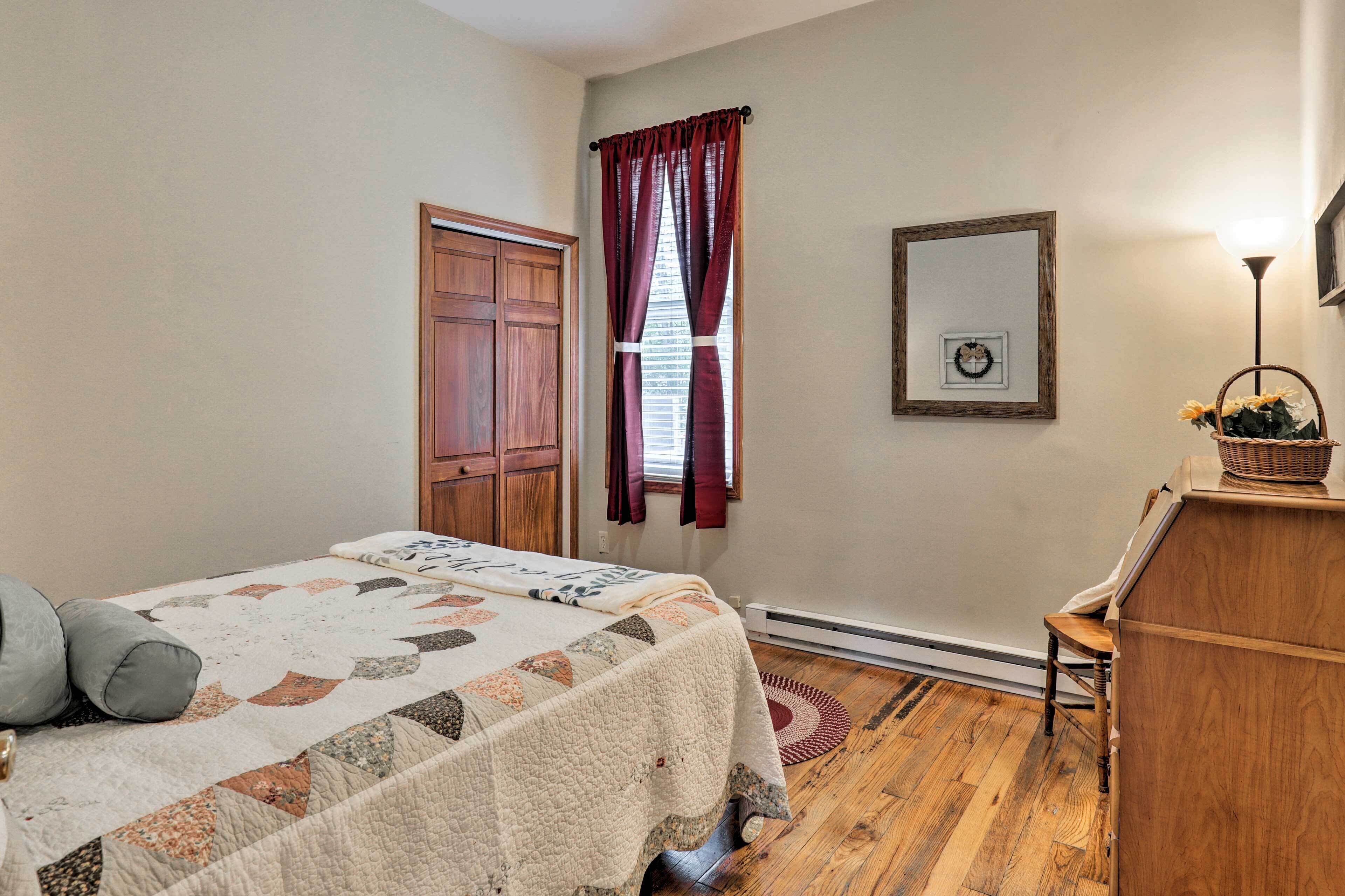 A bedroom with a bed, wooden floor, a dresser, a window with curtains, and a wall-mounted picture.