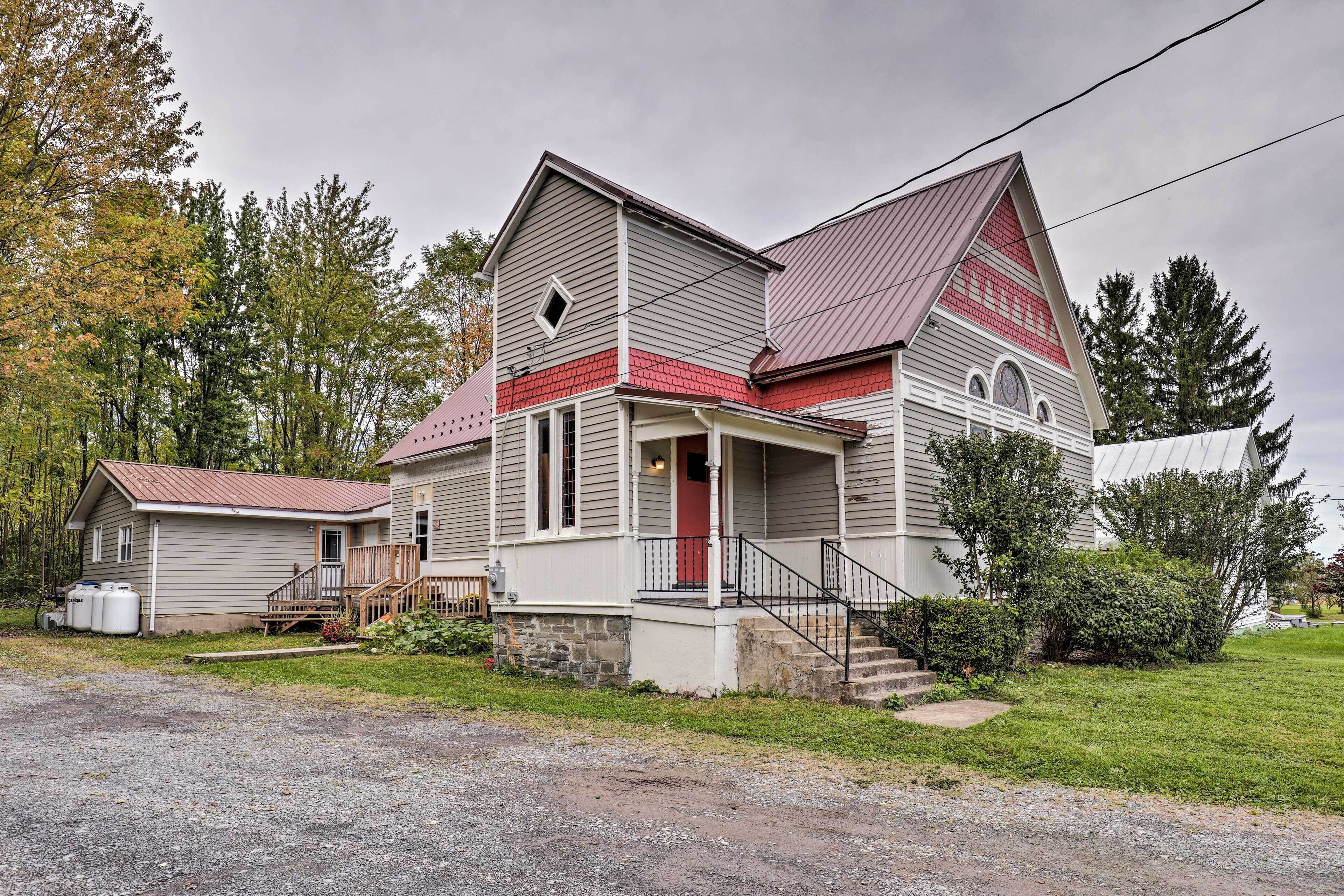A two-story house with a red door, a porch, and a stone foundation.