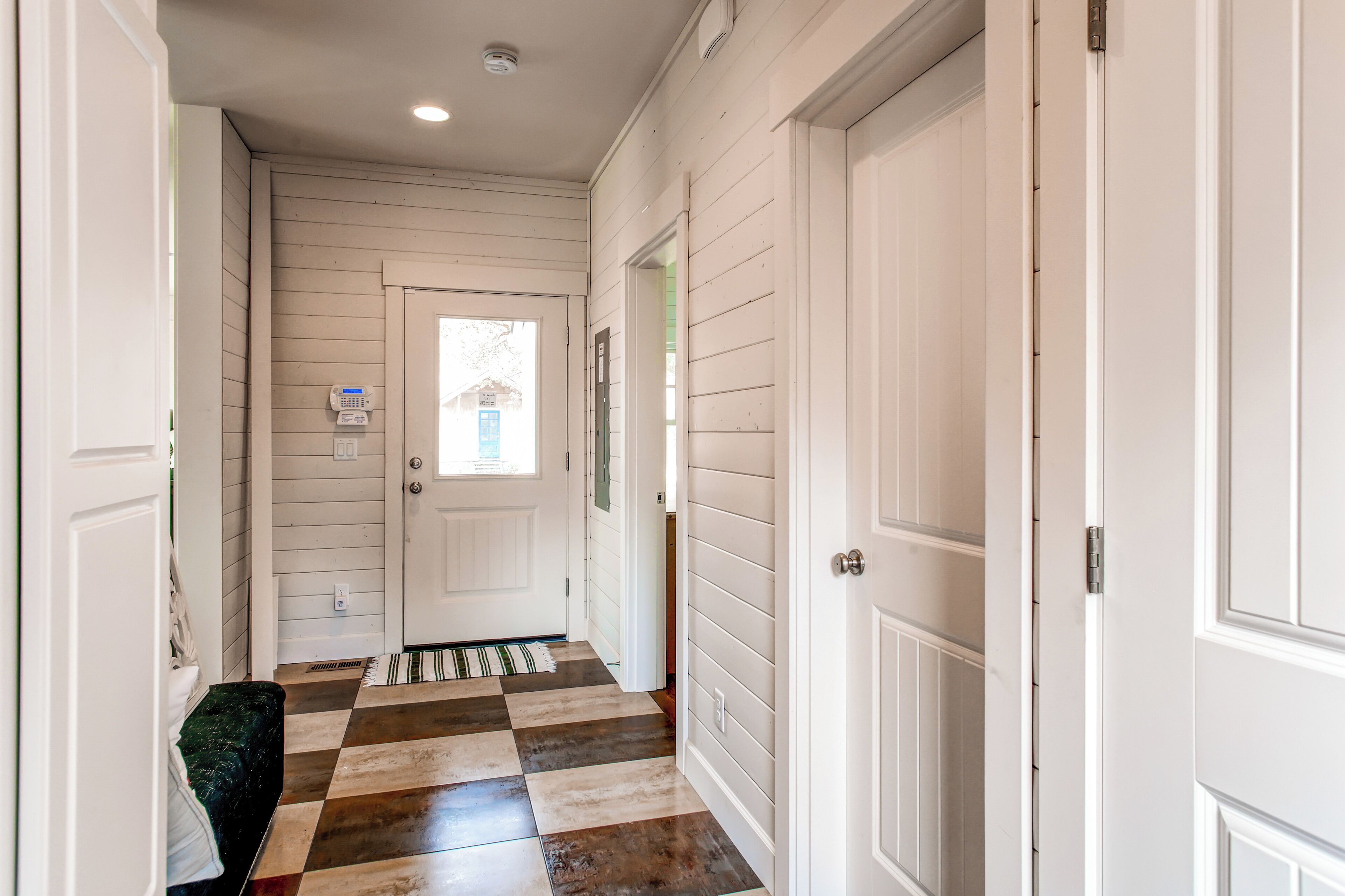 A hallway with white paneled walls, a checkered floor, and a door at the end.