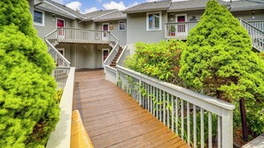 Une terrasse en bois menant à un bâtiment doté de plusieurs balcons et d’un escalier.