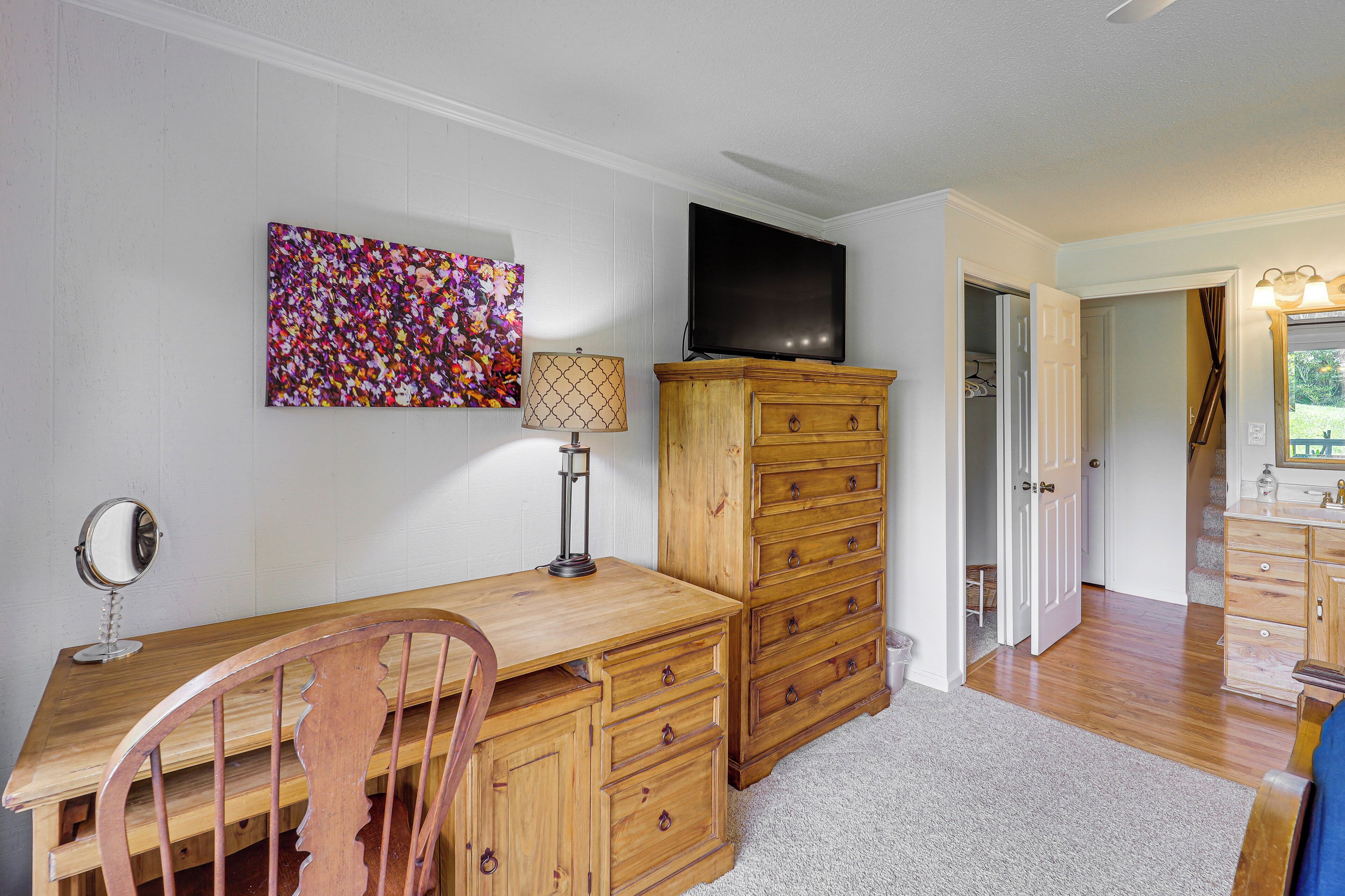 Une pièce avec un bureau en bois, une télévision, une commode et une œuvre d’art colorée accrochée au mur.