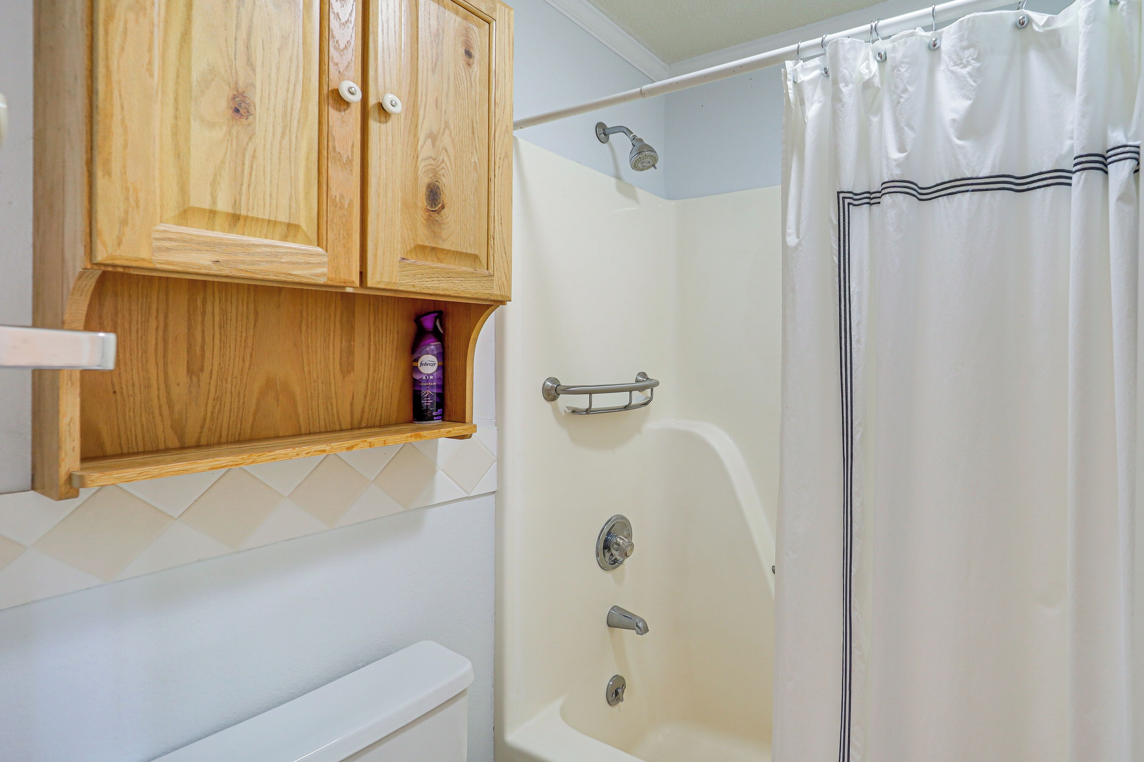A bathroom with a wooden cabinet, a shower with a curtain, and a toilet.
