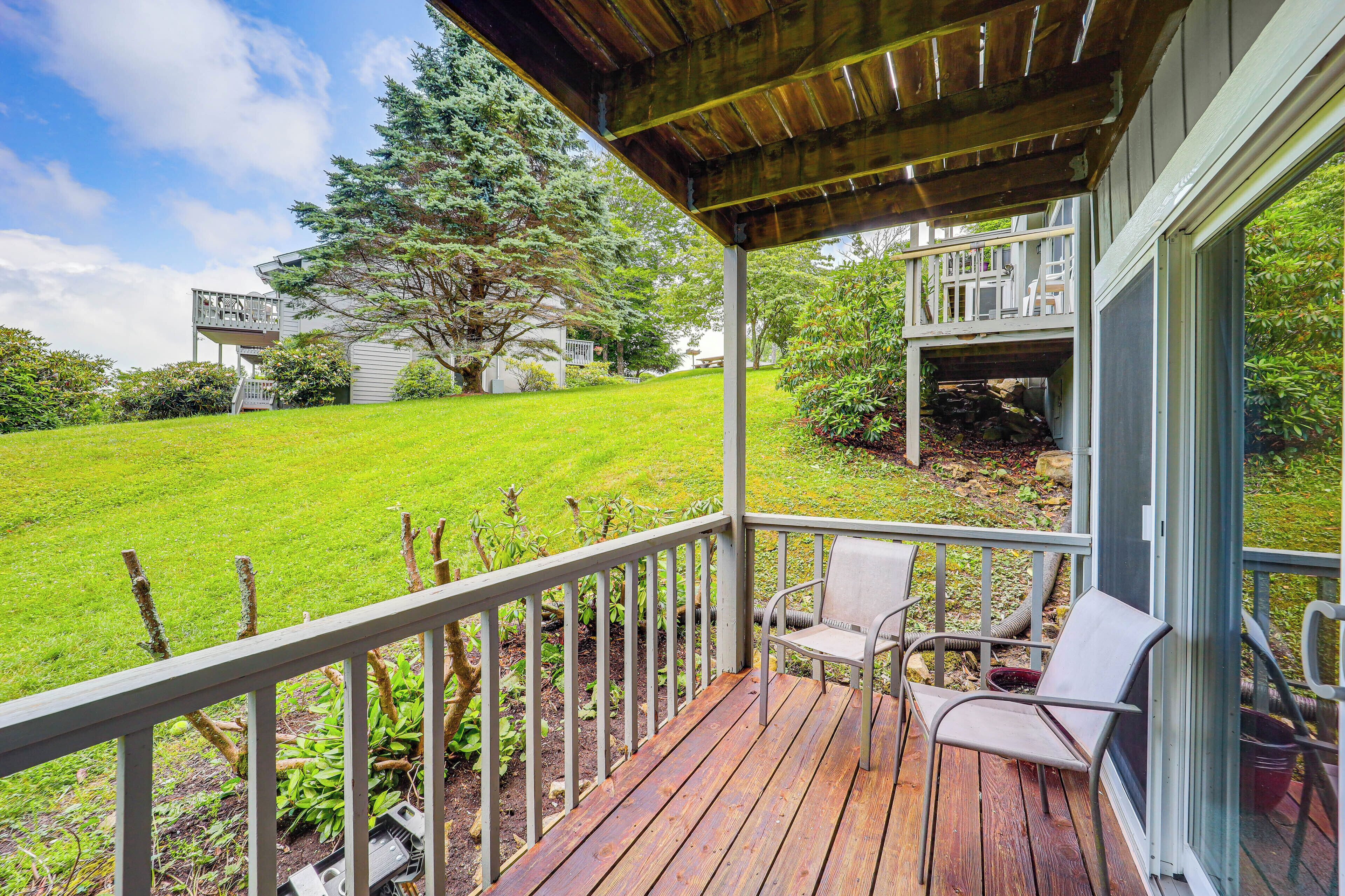 Une terrasse en bois avec des chaises, un espace abrité et une vue sur une pelouse verdoyante et des arbres.